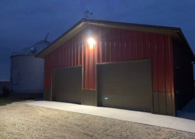 A barn with lights and a silo at night.