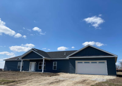 A blue house with a garage in the middle of a field.