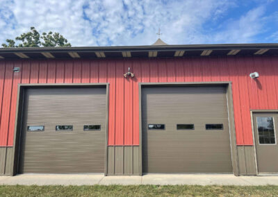 Two garage doors in a building with a red roof.