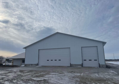 A white building with two garages in the middle of a snowy field.