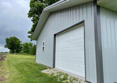 A garage with a white garage door and a grassy field.